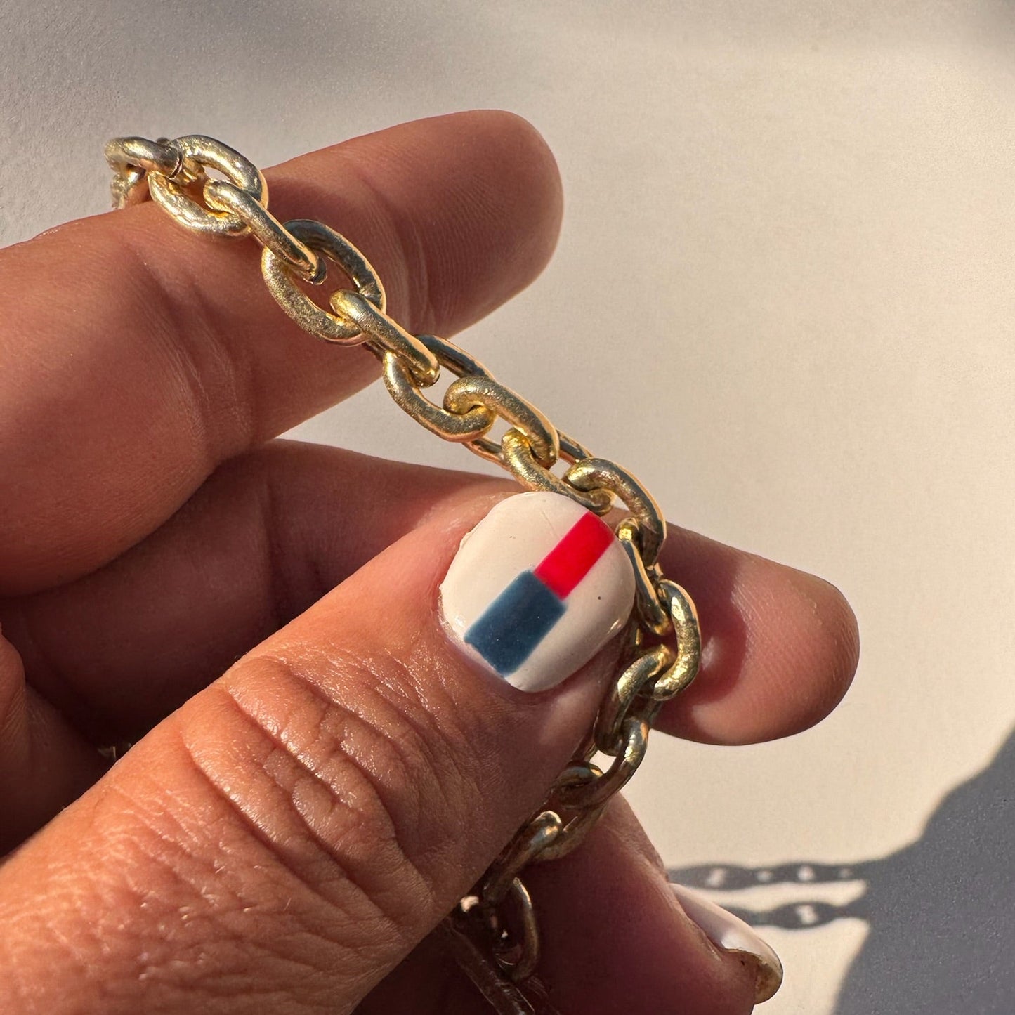 Gold chain bracelet held by a hand with a multicolored nail design.