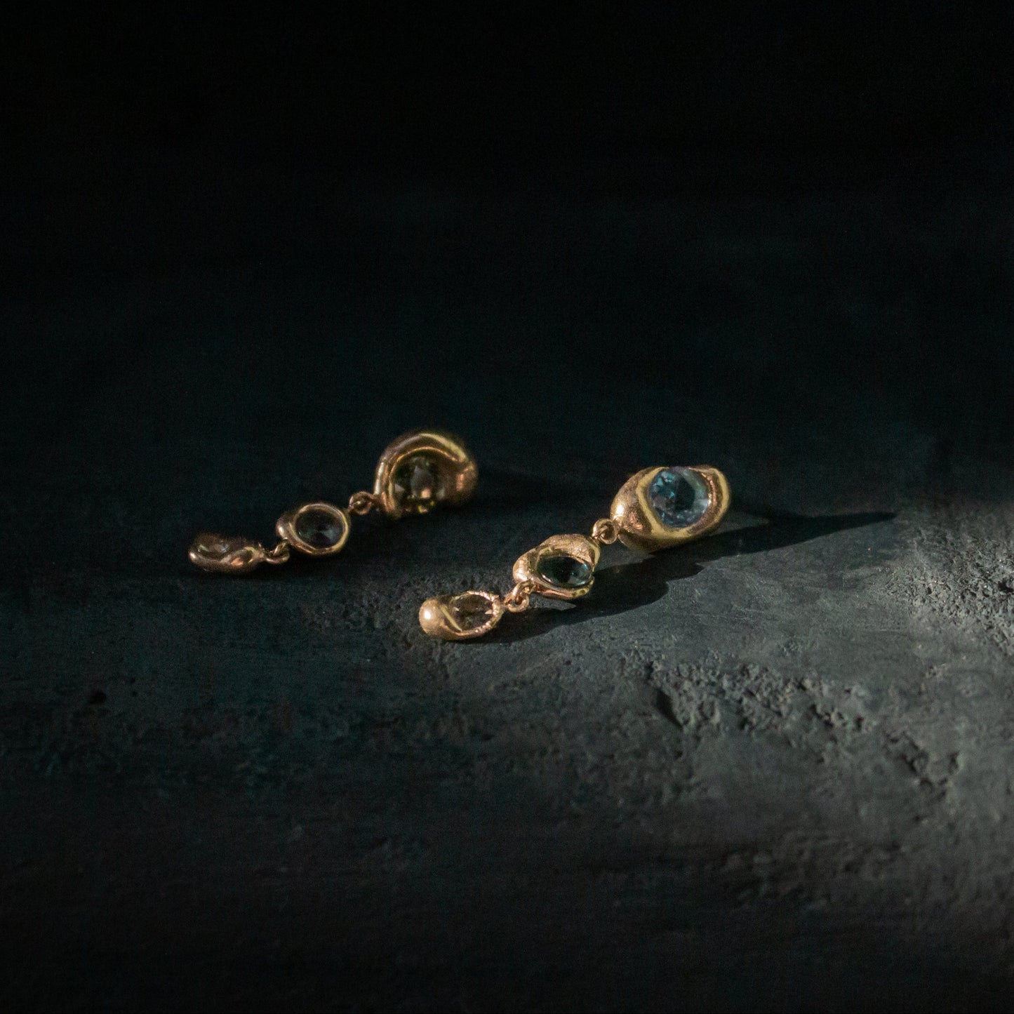 Gold earrings with gemstones on a dark textured surface